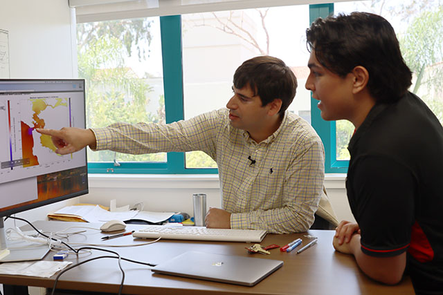 A student and professor confer in front of a computer screen