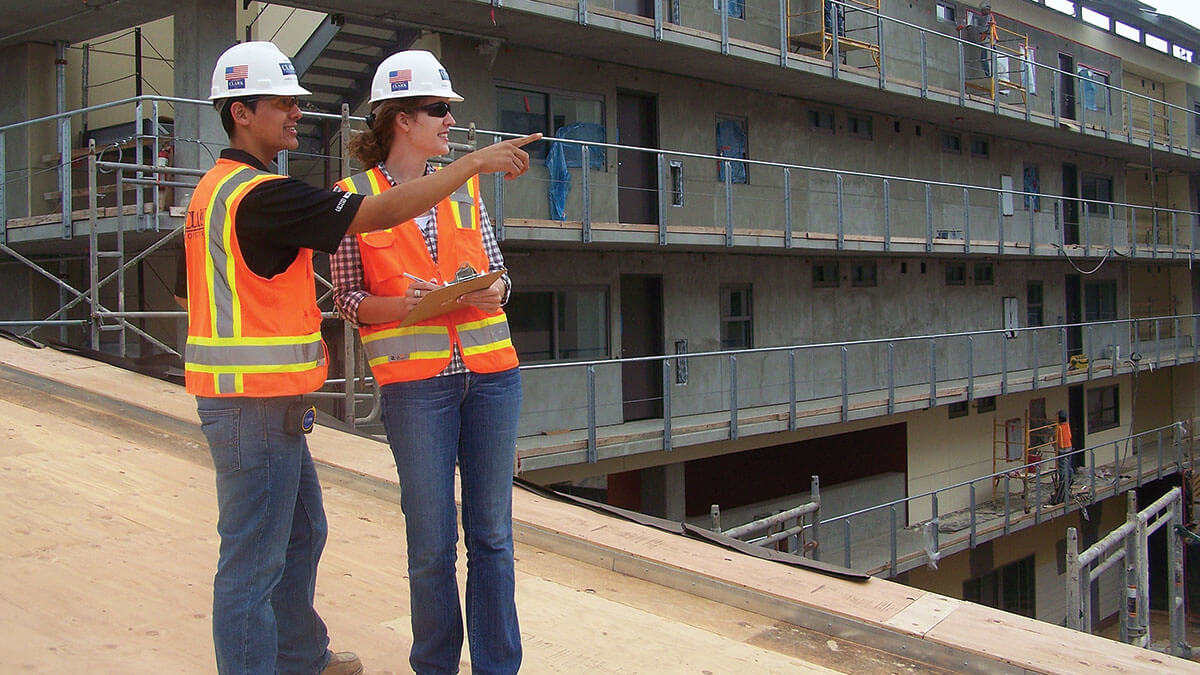 Two civil engineering students wearing hard hats on a construction site.